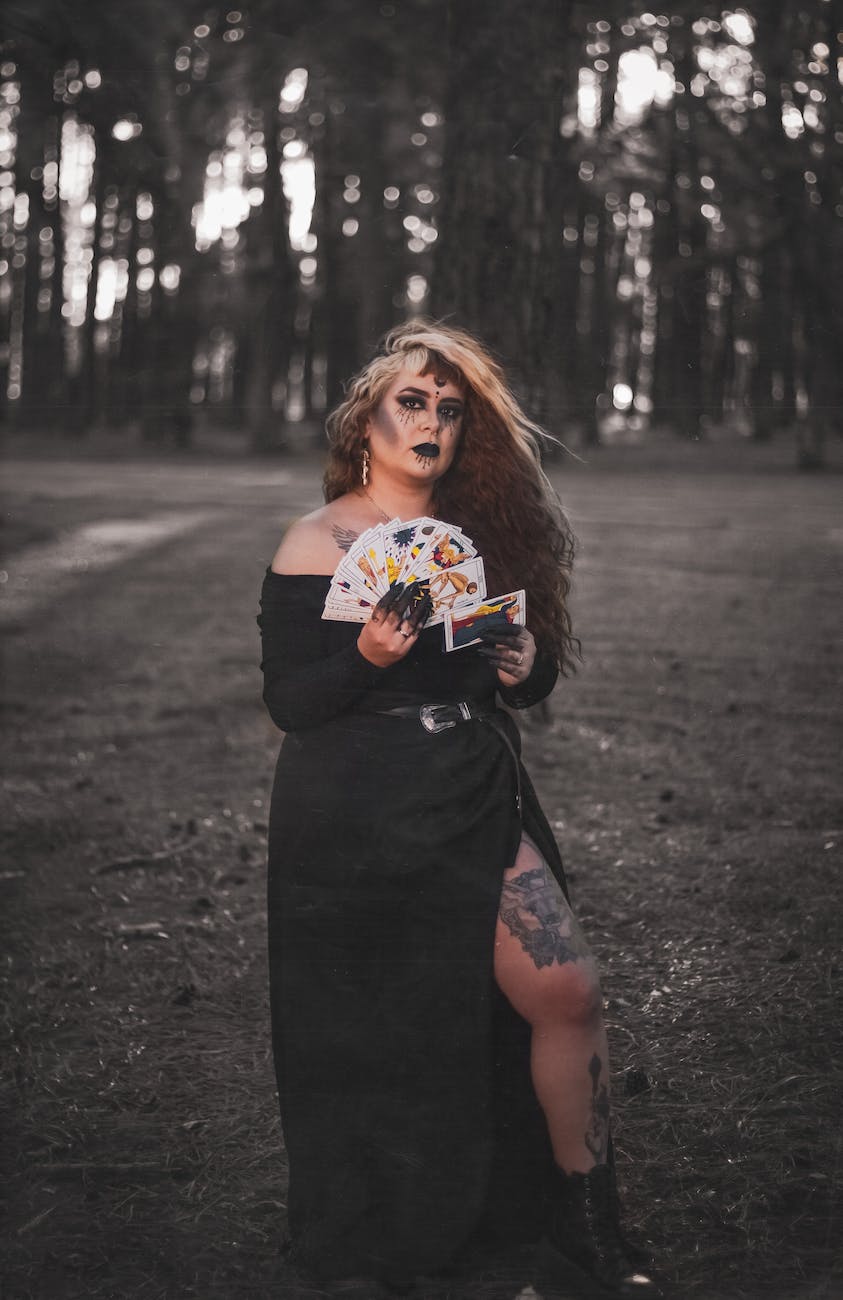 woman with long hair and tattoos holding a deck of cards in a forest