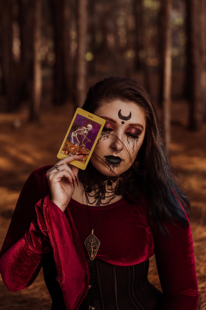 woman in a red dress wearing creative makeup holding a tarot card