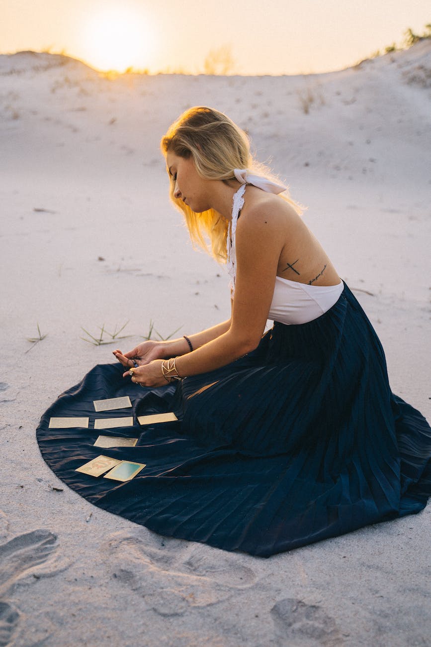 woman sitting on sand with tarot cards on her skirt