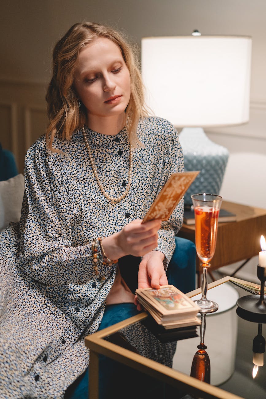 woman sitting on a couch in front of a table with champagne glass and looking at a tarot card